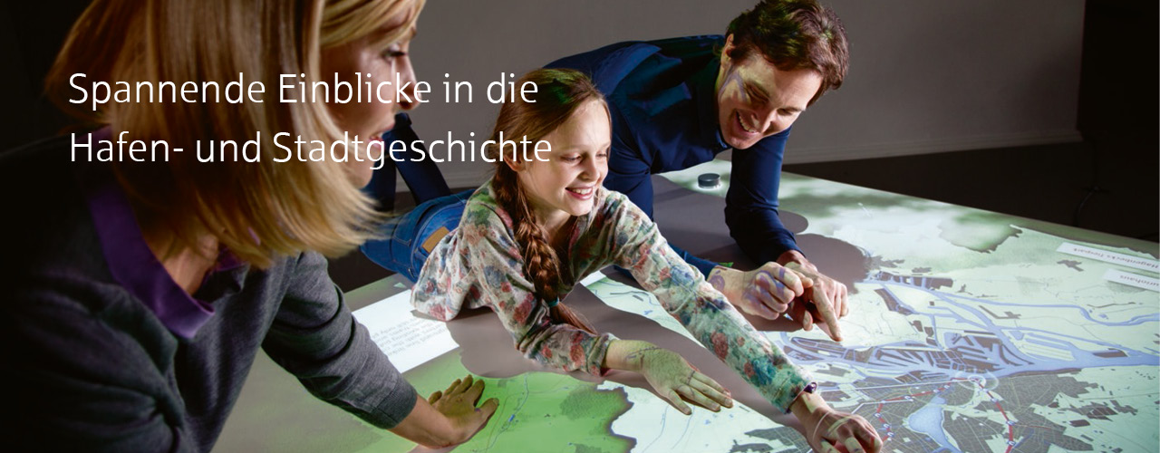 Familie bestehend aus Eltern und Kind lehnt ueber interaktiver Hamburger Stadtkarte im Hamburg Museum