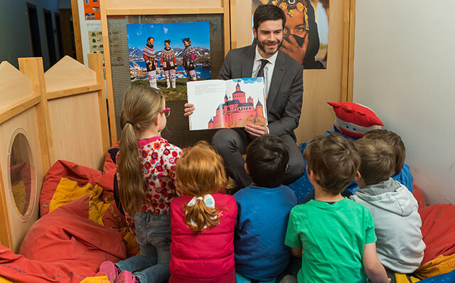 Mann in Anzug liest Kindergartengruppe aus einem Buch vor